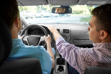 Wall Mural - driver courses and people concept - car driving school instructor teaching young man to drive