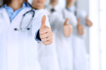 Wall Mural - Group of modern doctors standing as a team with thumbs up in hospital office. Physicians ready to examine and help patients. Medical help, insurance in health care, best desease treatment and medicine