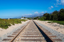 Railroad Tracks Converging In Perpective Into The Distance Towards Distant Mountains