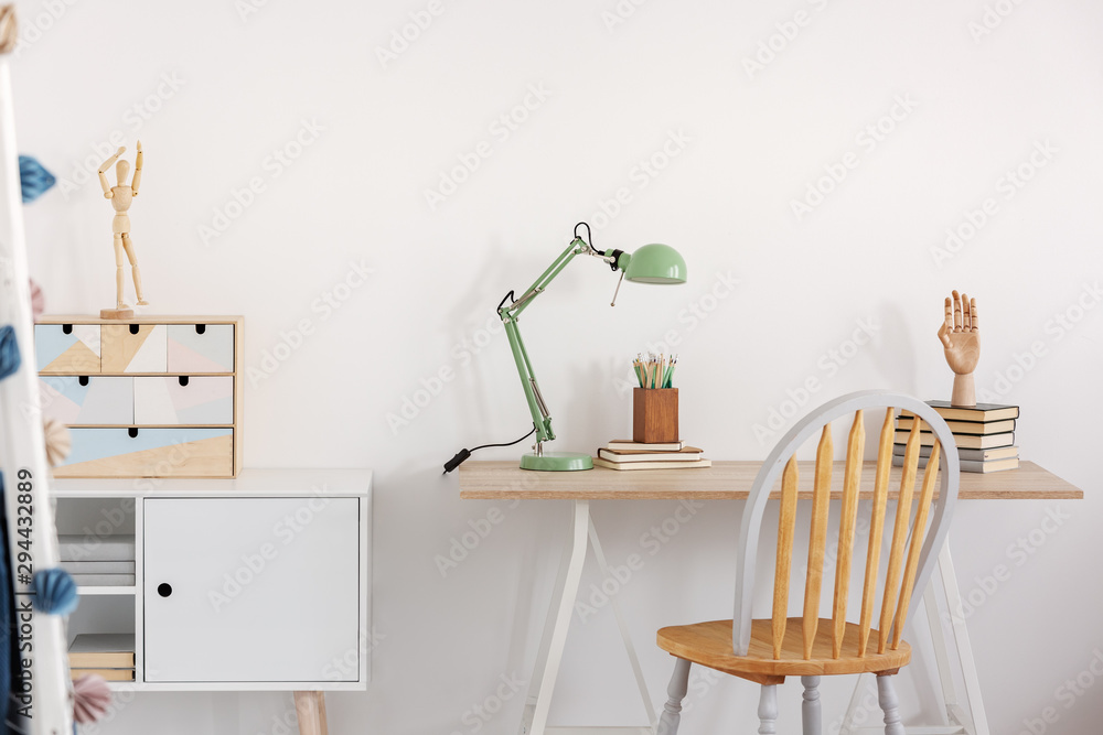 Pile of books, wooden hand and industrial mint colored lamp on stylish wooden desk in white kid's bedroom - obrazy, fototapety, plakaty 