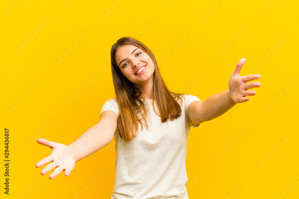 young pretty woman smiling cheerfully giving a warm, friendly, loving welcome hug, feeling happy and adorable against orange background - obrazy, fototapety, plakaty 