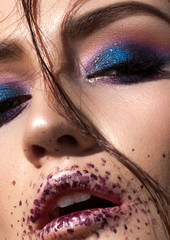 Close up photo. Beautiful young model with professional creative colorful makeup. Blue smoky eyes, lilac spots on lips.