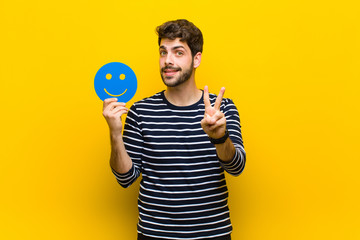 young handsome man holding a smiling face against orange backgro