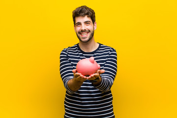 young handsome man holding a piggy bank against orange backgroun