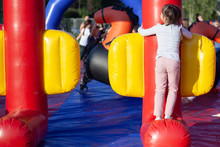 A Child On An Inflatable Playground. Amusement Park For Children. Inflatable Trampoline For Jumping And Fun. Rest In The Summer In The Fresh Air. The Kid Keeps His Balance On The Inflatable Structure.