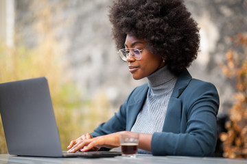 Wall Mural - professional young black businesswoman sitting outside with laptop