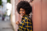 Fototapeta Uliczki - smiling young african american woman with afro hair standing outside and holding glasses