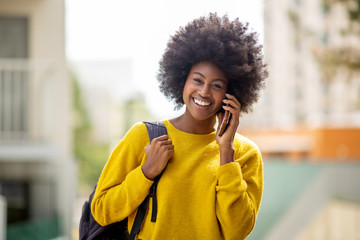 Wall Mural - smiling african american woman talking with mobile phone outside in city