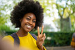 beautiful young afro american woman taking selfie with peace hand sign outdoors