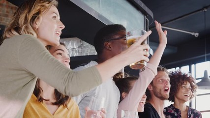 Wall Mural - Group Of Male And Female Friends Celebrating Whilst Watching Game On Screen In Sports Bar