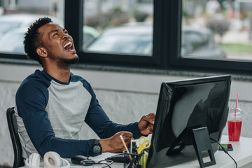 angry african american programmer gesturing while sitting at workplace in office