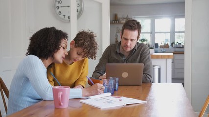 Wall Mural - Father Works On Laptop As Mother Helps Son With Homework On Kitchen Table