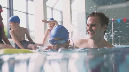 Wall Mural - Male Swimming Coach Giving Boy Holding Float Lesson In Pool