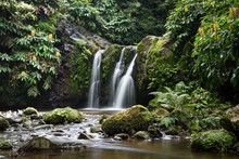 Natural Waterfall Surrounded By Rocks And Foliage At The Parque Natural Da Ribeira Dos Caldeirões, São Miguel Island, Azores. Rocks In The Meandering River Are In The Foreground. Long Exposure Image.