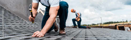 Fotomural panoramic shot of handyman holding hammer while repairing roof near coworker