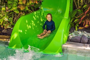 Wall Mural - Happy boy on water slide in a swimming pool having fun during summer vacation in a beautiful tropical resort