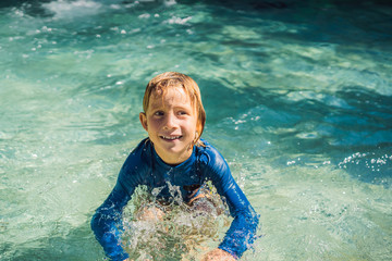 Wall Mural - Happy boy on water slide in a swimming pool having fun during summer vacation in a beautiful tropical resort