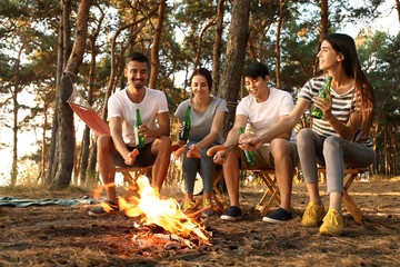 Poster - Young friends roasting sausages on fire and drinking beer at camp