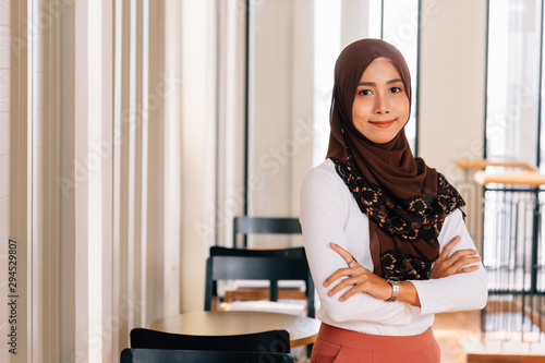 Cuadros en Lienzo Young happy and successful South East Asian Islamic business woman with arms crossed in business corporate building setting looks at camera