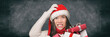 © Maridav - Christmas stress holiday shopping woman in santa hat stressed funny expression on black blackboard banner panorama. Anxious lady shopper late for christmas gifts stressing about the budget spending.