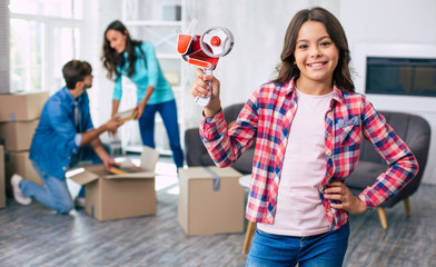 Wall Mural - Ready for work. Cute youngster is holding a scotch tape in her hand, ready to help her parents to pack or unpack their personal items in their new apartment.