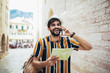 Handsome bearded tourist with backpack is making travel across city, using phone.