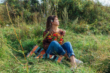 Beautiful woman with camomile flower in hair sitting on the grass and drinking tea outdoors