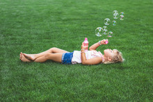 Little Girl Laying On The Grass, Blowing Soap Bubbles