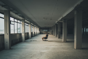 Man sitting in front of a large window in an empty hall of an abandoned building