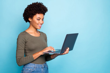 Wall Mural - Portrait of positive cool confident afro american girl freelancer use laptop type emails chat with her partners business clients wear green style clothes denim jeans isolated blue color background