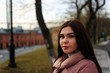 © Николай Крапивин - Young cute pregnant girl in pink warm down jacket posing on the background of cable-stayed bridge, trees and brick buildings. Late autumn, the cold is coming.