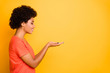 © deagreez - Copyspace side profile photo of cheerful cute charming nice girlfriend holding something with her hands looking at it wearing orange t-shirt isolated over yellow vibrant color background