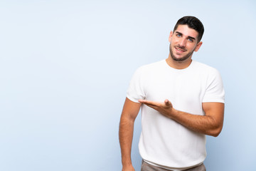 Caucasian handsome man over isolated blue background presenting an idea while looking smiling towards