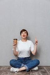 Wall Mural - Image of woman pointing finger upward sitting on floor with coffee cup