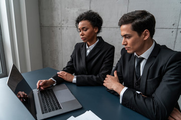 two young diverse business partners discussing work in loft office. woman is pointing at laptop. con