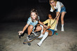 © Drobot Dean - Image of cheerful multiethnic girls smiling and riding skateboards at night