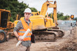 © Pituk - Caucasian handsome engineer stand holding a laptop and roll of paper on road construction site.