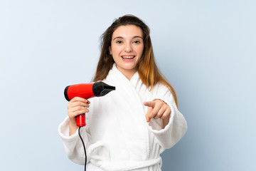 Young woman in a bathrobe with hair hairdryer points finger at you with a confident expression