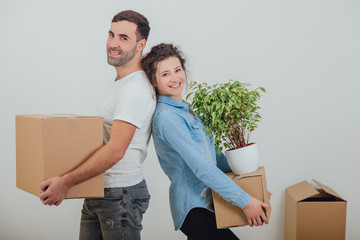 Happy wife and husband holding carton boxes, standing back to back, smiling extremely satisfied to move into new apartment.