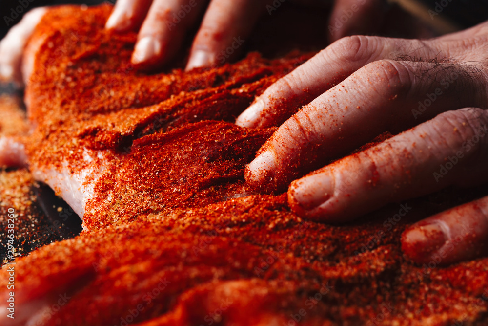 Man preparing raw piece of meat, rubbing different spices and herbs in it before roasting - obrazy, fototapety, plakaty 