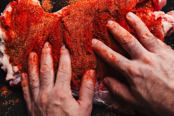 Man preparing raw piece of meat, rubbing different spices and herbs in it before roasting