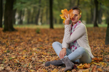 Short-cut autumn woman in autumn park has fun playing with fallen leaves in jeans and a light autumn blouse