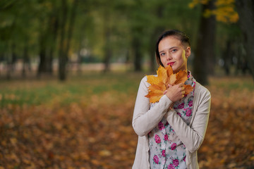 Short-cut autumn woman in autumn park has fun playing with fallen leaves in jeans and a light autumn blouse