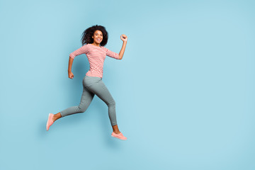 Wall Mural - Full length body size side profile photo of cheerful excited cute nice curly wavy youngster running jumping for sales wearing trousers pants striped t-shirt sneakers isolated over pastel blue color