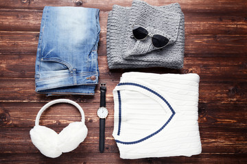 Wall Mural - Knitted sweater with scarf, jeans, earmuffs, sunglasses and wrist watch on wooden table
