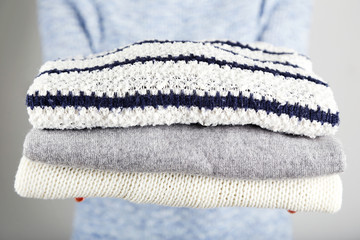 Female hands holding folded knitted sweaters on grey background