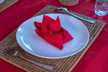 Wall Mural - Elegant table setting with fork, spoon, white plate and red napkin in restaurant . Nice dining table set with arranged silverware and napkins