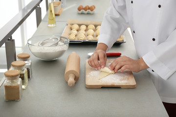 Wall Mural - Female pastry chef preparing croissant at table in kitchen, closeup