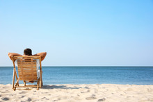 Young Man Relaxing In Deck Chair On Sandy Beach
