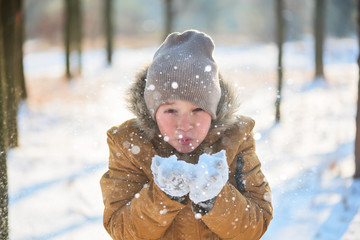 Wall Mural - Boy in a warm jacket, hat and gloves throws snowballs over himself in a winter park